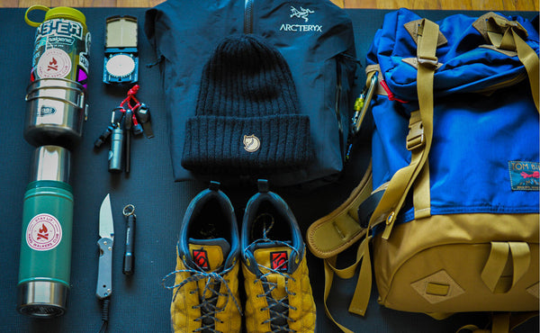 A Guide's Pack loadout photo with the Guide's Pack, a pair of shoes, a jacket and beanie, a pair of water bottles, a compas, a pocket knife and pocket flashlight, and various tools.